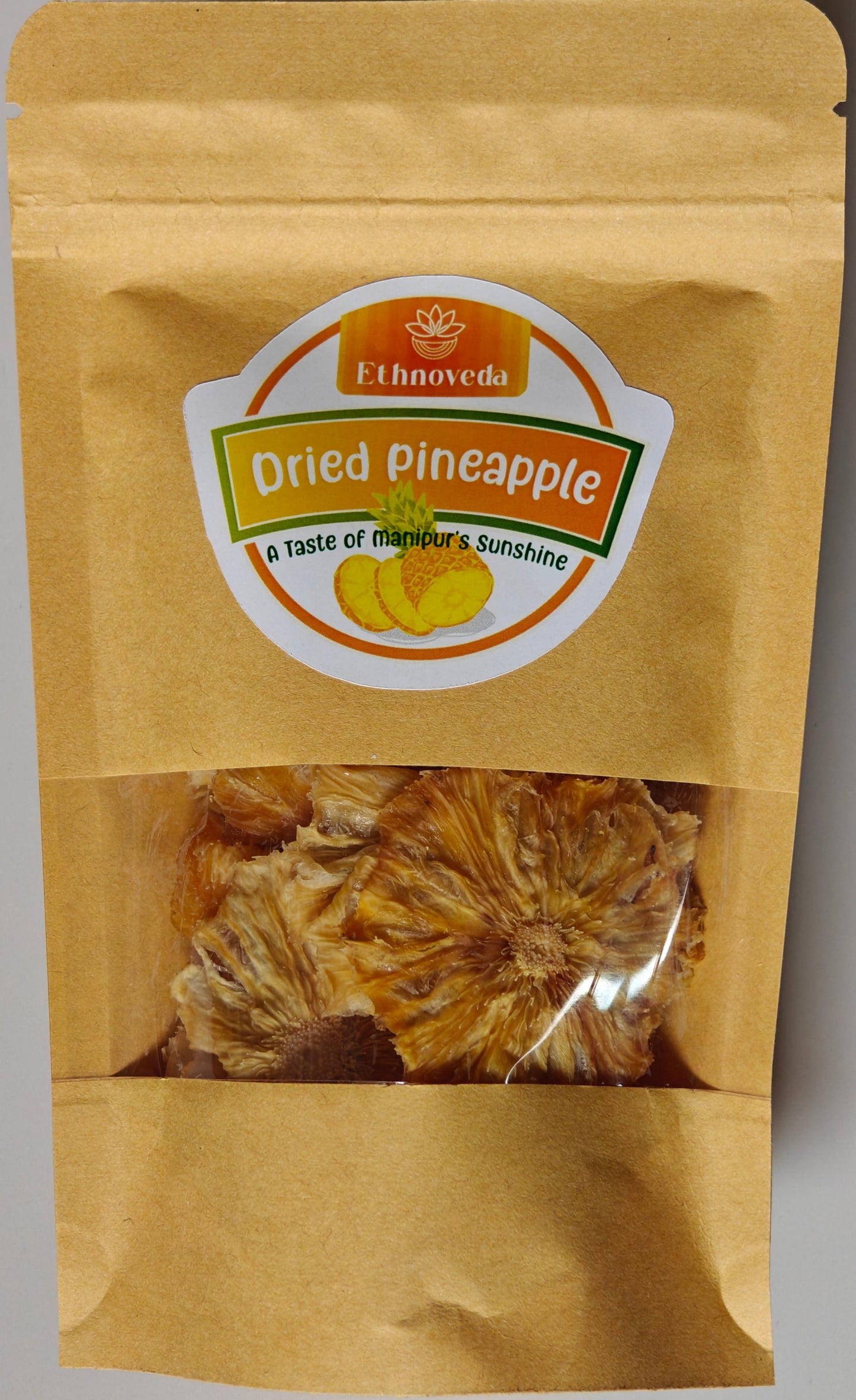 Kraft paper packaging of dried pineapple with Ethnoveda label on a gray background